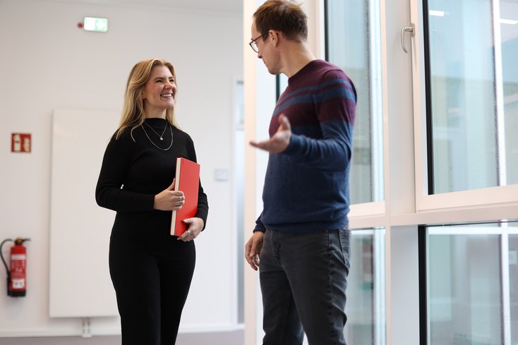 Zwei Personen unterhalten sich auf dem Flur im Vorbeigehen.