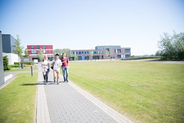 Drei Studierende gehen auf einem Weg vor dem Hochschulgebäude