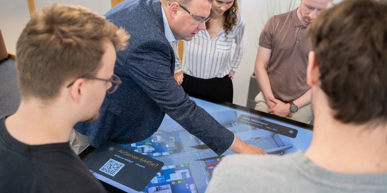 Professor erklärt Studierende etwas auf einem Touchscreen-Monitor.
