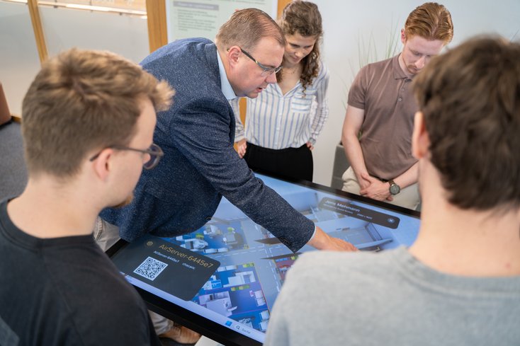 Professor erklärt den Studierenden etwas auf einem Touchscreen Monitor