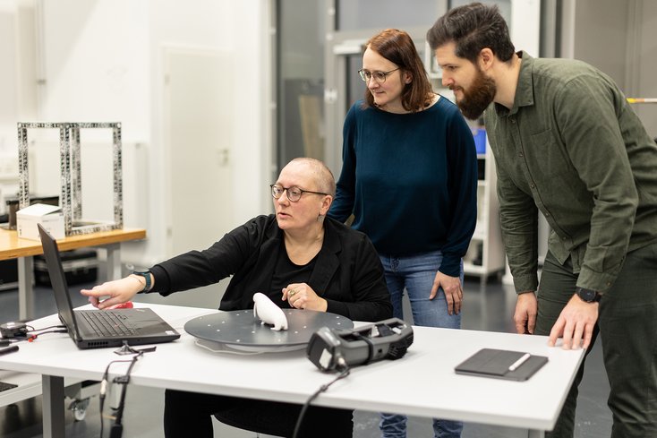 Drei Personen befinden sich im Mess-Labor und tauschen sich aus.