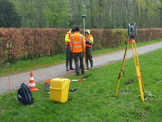 Studierende stehen zusammen und halten Lotstab mit GNSS zur topographischen Vermessung des Geländes, im Vordergrund steht ein Tachymeter und Equipment