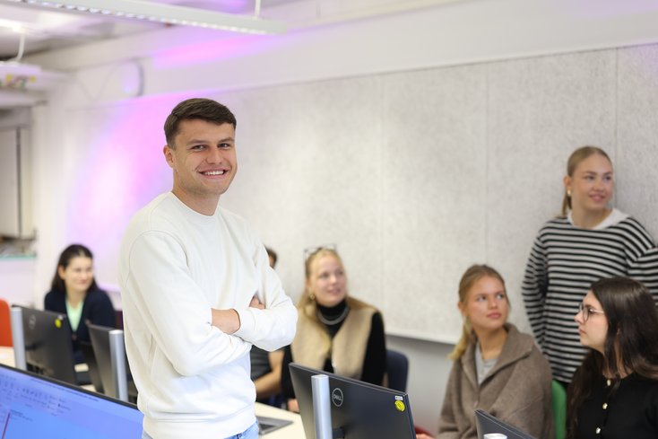 Student lächelt in die Kamera, Kommilitonen im Hintergrund.