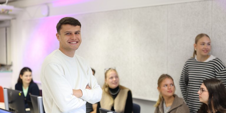 Student lächelt in die Kamera, Kommilitonen im Hintergrund.