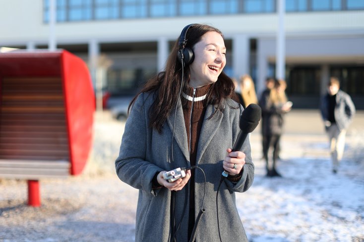 Studentin mit Mikrofon und Kopfhörer, im Hintergrund das Hauptgebäude der Jade Hochschule in Wilhelmshaven und ein roter Strandkorb