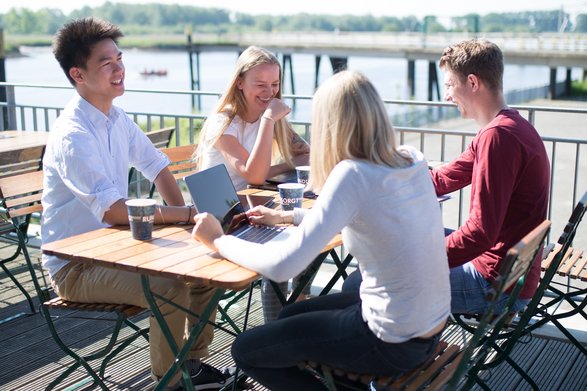 Vier Studierende sitzen lachend an einem Tisch auf der Terrasse der Mensa.