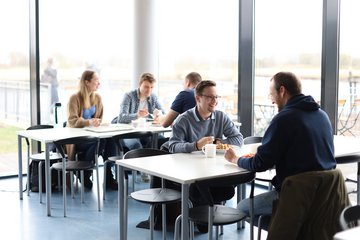 Studierende sitzen beim Essen an Tischen in der Mensa.