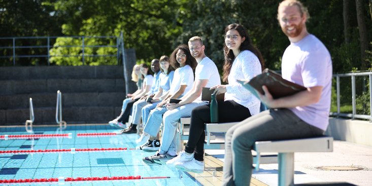 Personen sitzen an einem Schwimmbecken