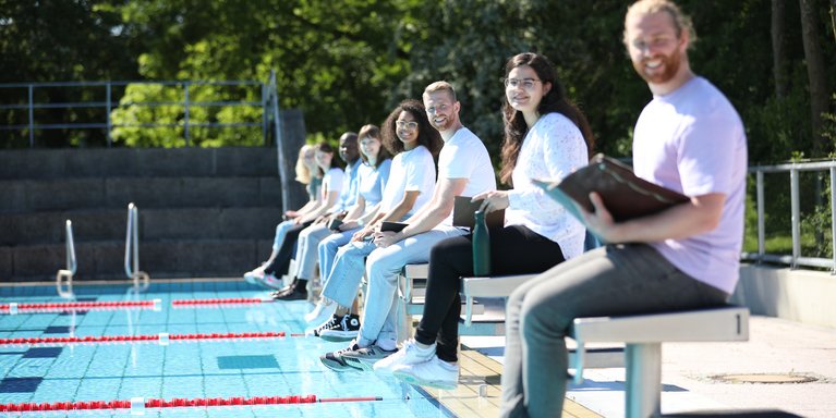 Personen sitzen an einem Schwimmbecken