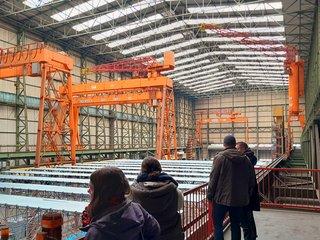 Studierende stehen in einer Halle und schauen bei der Produktion zu.