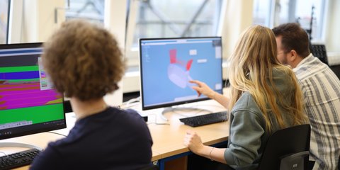 Studierende diskutieren am Rechner.