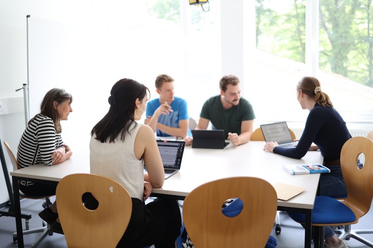 Dozentin erklärt kleiner Studierendengruppe etwas am Laptop.