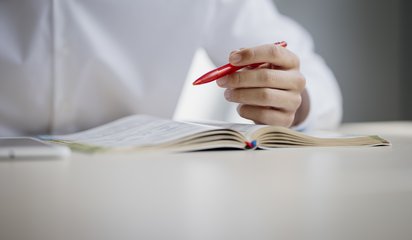 Jemand sitzt an einem Tisch und studiert ein Lehrbuch.