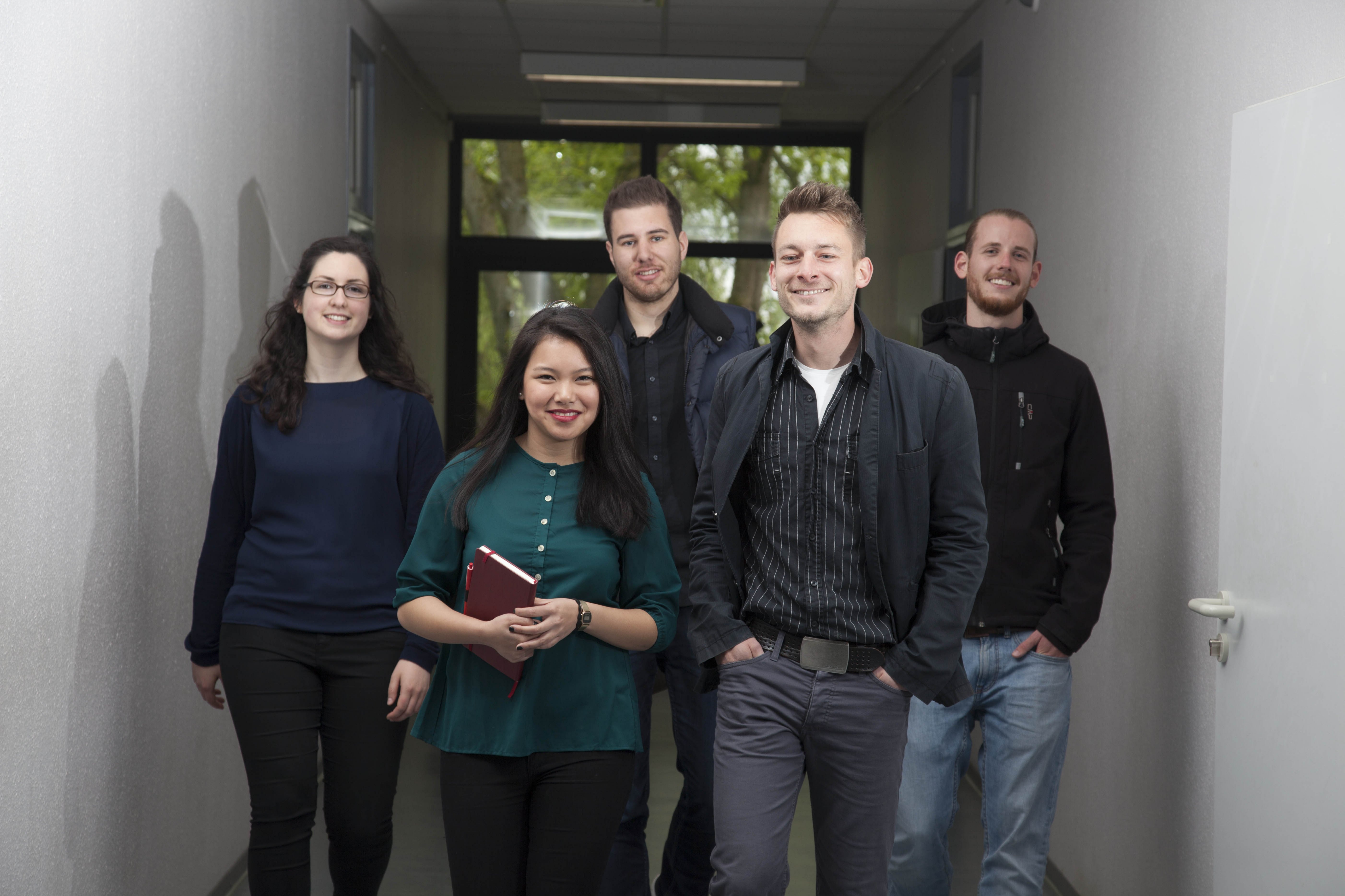 Gruppe von fünf weiblichen und männlichen Studierenden laufen einen Flur entlang.