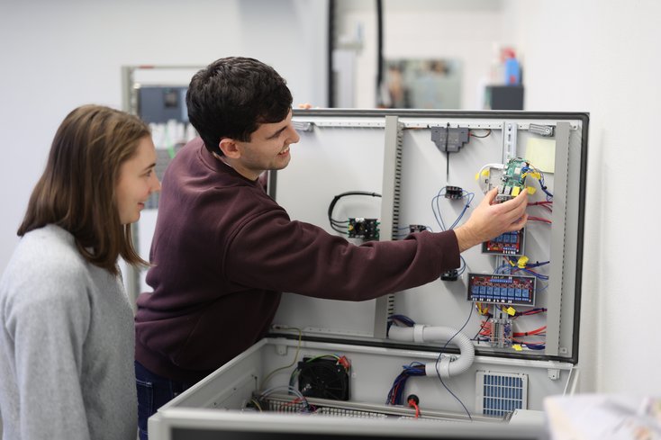 Zwei Studierende stehen an einem Koffer mit Steuerungstechnik.
