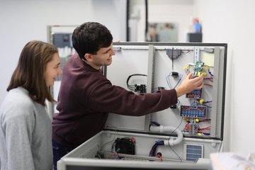 Zwei Studierende stehen an einem Koffer mit Steuerungstechnik.