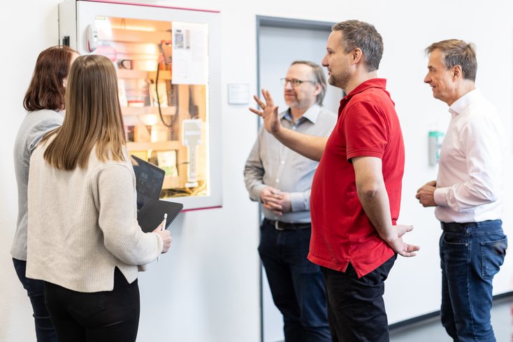 Studierende und Dozenten stehen vor einem SmartHome-Schrank und der Dozent erklärt.