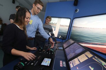 Drei Studierende stehen vor der Brücke im Schiffsführungssimulator