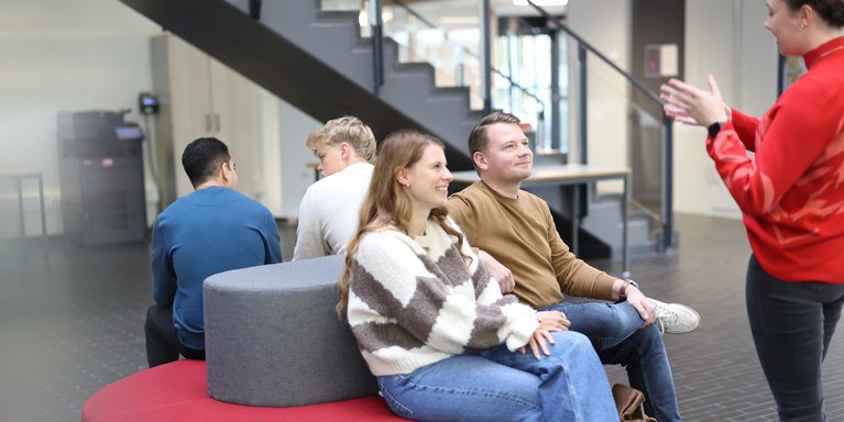 Studierende sitzen auf den Sofas im Lichthof der Hochschule und bekommen etwas erklärt