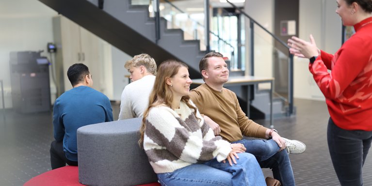 Studierende sitzen auf den Sofas im Lichthof der Hochschule und bekommen etwas erklärt