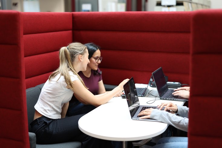 Studentinnen unterhalten sich in der Bibliothek.