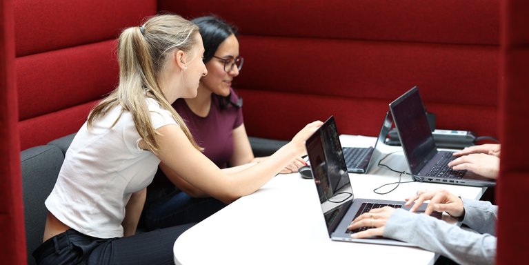 Studentinnen unterhalten sich in der Bibliothek.