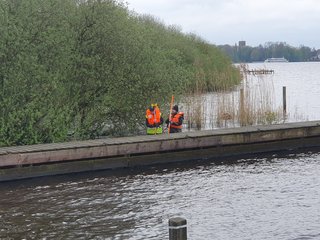 Studierende stehen im Wasser und messen die Tiefe mit Lotstab und Prisma über einen Tachymeter an Land