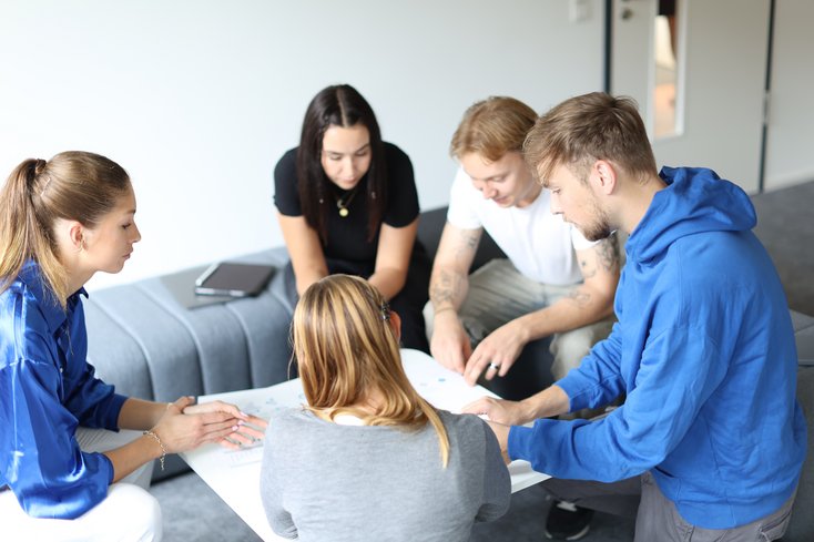 Eine Gruppe Studierender bespricht etwas am Plan im Sitzen.