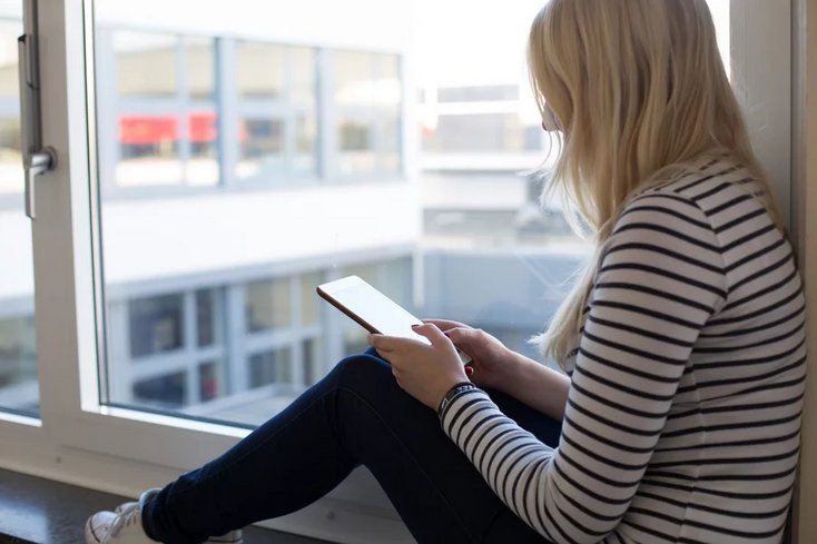 Studierende sitzt an einem Fenster und blickt auf ein Tablet.