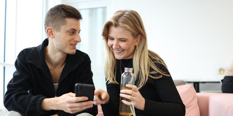 Ein Student erklärt seiner Kommilitonin etwas am Smartphone.