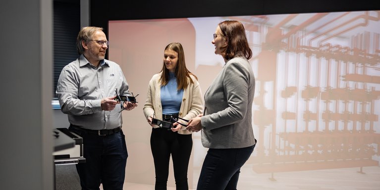 Drei Personen stehen in einem Virtual Reality Raum und diskutieren.