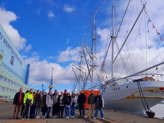 Gruppenbild neben einem Segelschiff bei sonnigem Wetter. 