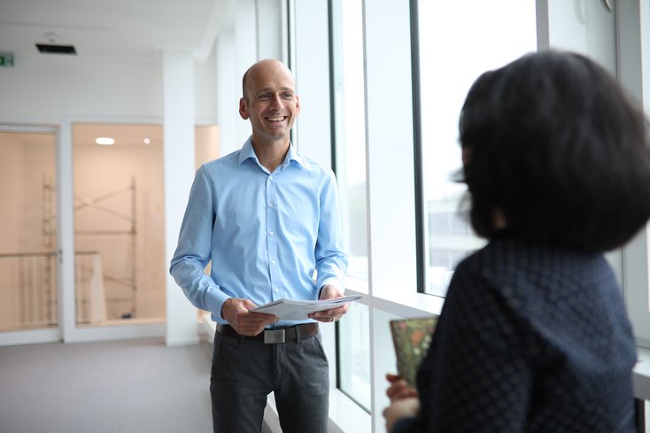 Lächelnder Mann und Frau in Rückenansicht sichtbar, unterhalten sich auf dem Flur.