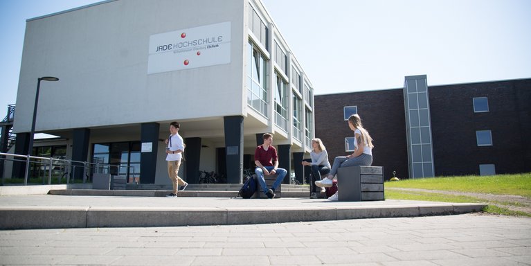 Studierende sitzen bzw. stehen vor dem Hochschulgebäude