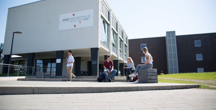 Studierende sitzen bzw. stehen vor dem Hochschulgebäude