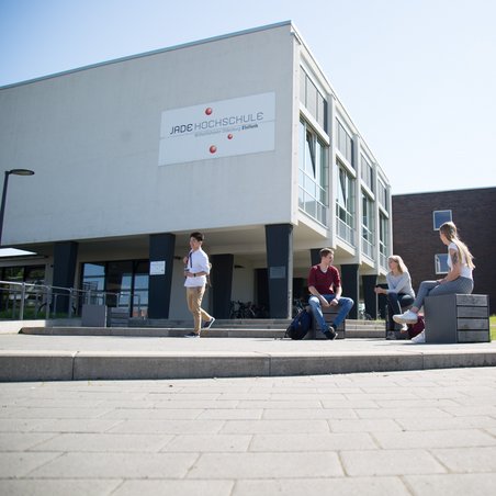 Studierende sitzen bzw. stehen vor dem Hochschulgebäude