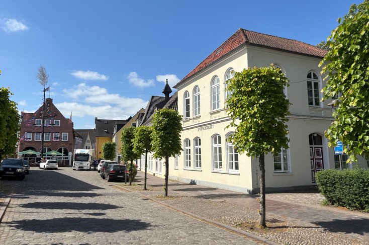 Sonniger Blick auf den Rathausplatz Elsfleth mit Bäumen; rechts das Alte Amtsgericht Elsfleth, im Hintergrund das Restaurant Kogge.