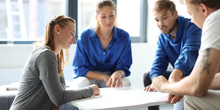 Eine Gruppe Studierender sitzt einer niedrigen Tischgruppe und bespricht etwas.