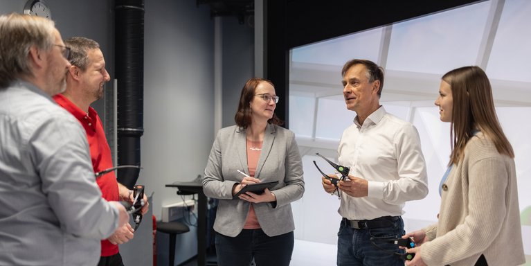 Männer und Frauen diskutieren in einem Virtual Reality Raum und halten Shutterbrillen in den Händen.
