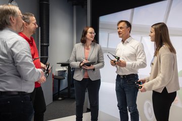 Männer und Frauen diskutieren in einem Virtual Reality Raum und halten Shutterbrillen in den Händen.