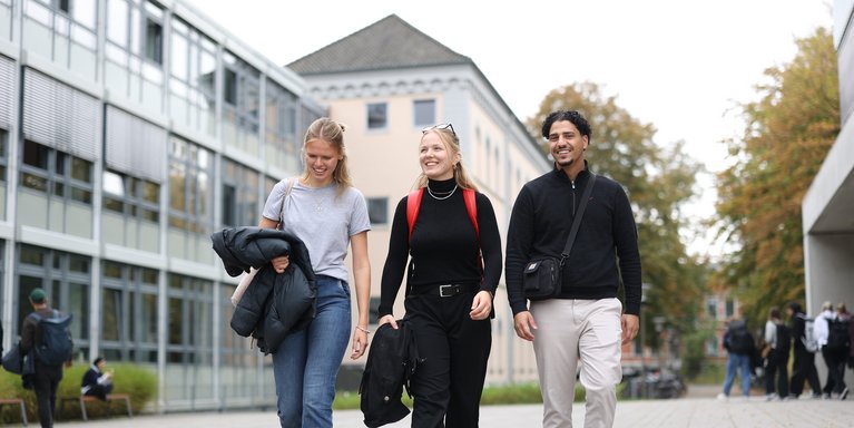 Drei Studierende gehen über den Campus