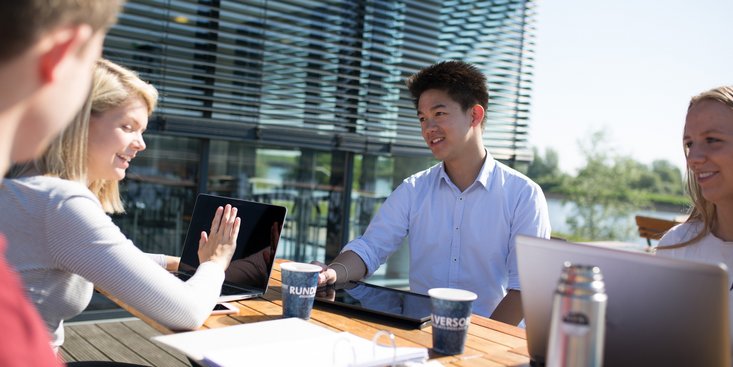 Studierende sitzen an einem Tisch vor der Mensa
