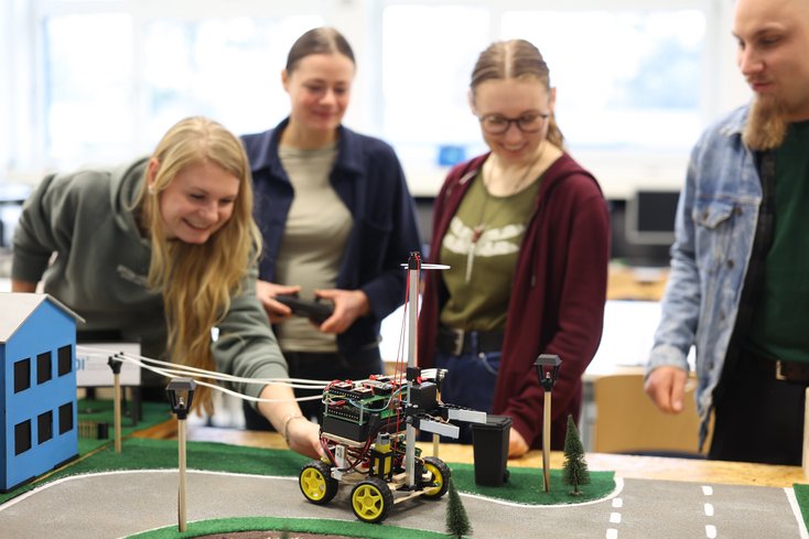 Studierende stehen an einem Straßenmodell und lassen einen selbstgebautes Roboterfahrzeug fahren.
