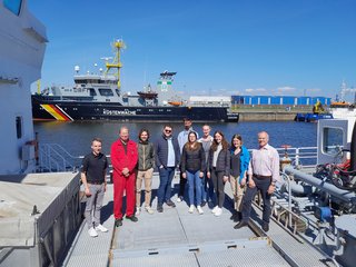 Studierende stehen im Hafen in Cuxhaven. Im Hindergrund ist ein Schiff von der Küstenwache zu sehen.
