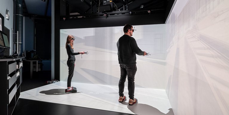 Zwei Personen, die mit VR-Brillen und Kontrollern ausgestattet sind, arbeiten im Labor für digitales Engineering.