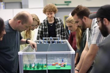Eine Gruppe Studierender steht mit dem Dozenten um ein Wellenbecken herum, in dem gerade ein Experiment durchgeführt wird.