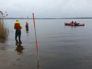 Studierende messen mit Lotstab die Tiefe im Uferbereich vom Boot aus