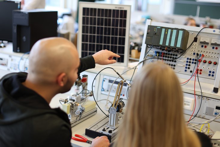 Zwei Studierende sitzen vor Steuerungsmodul und besprechen etwas.