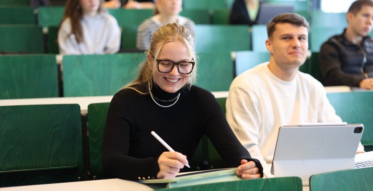 Studierende sitzen im Vorlesungssaal und machen Notizen.