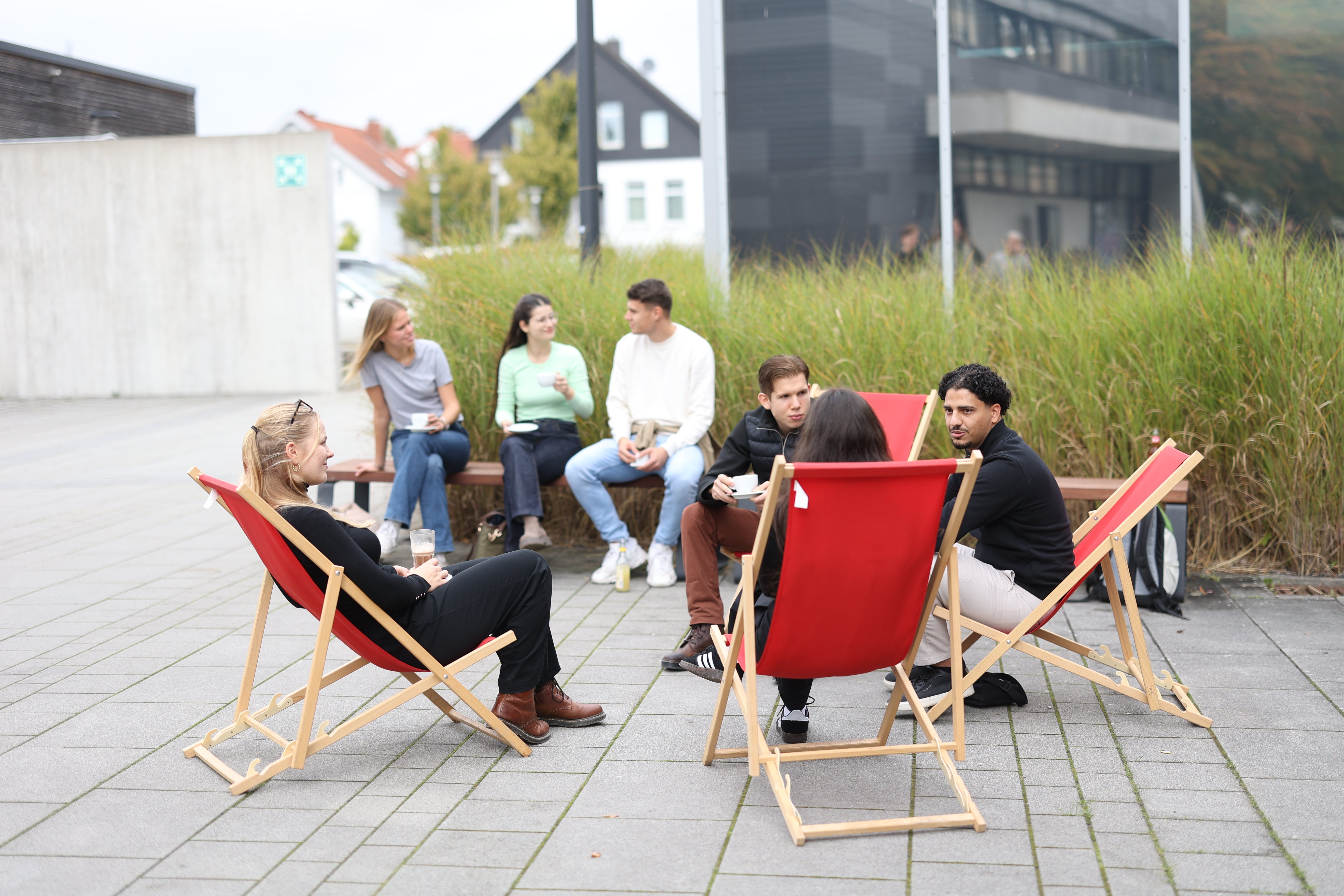 Studierende sitzen vorm Campuscafé und unterhalten sich.